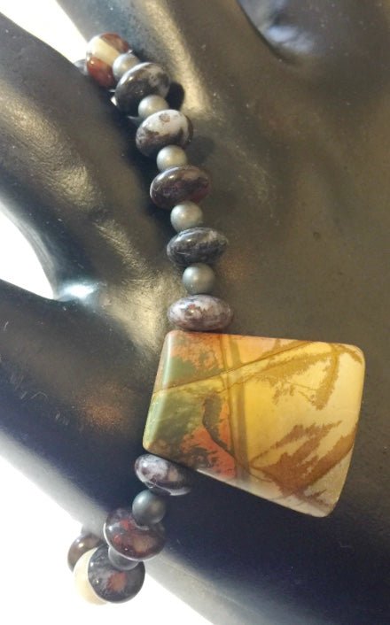 Crafted with an array of semi-precious stones in hues of brown, green, gray, white, red, and orange, this handmade jewelry piece is sure to make a stylish statemen